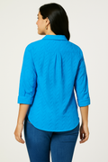 Back view of the Jaclyn Smith Embroidered Cotton Voile Buttoned Shirt in bright blue, featuring a chevron texture and 3/4-length sleeves, styled with medium-wash denim jeans.
