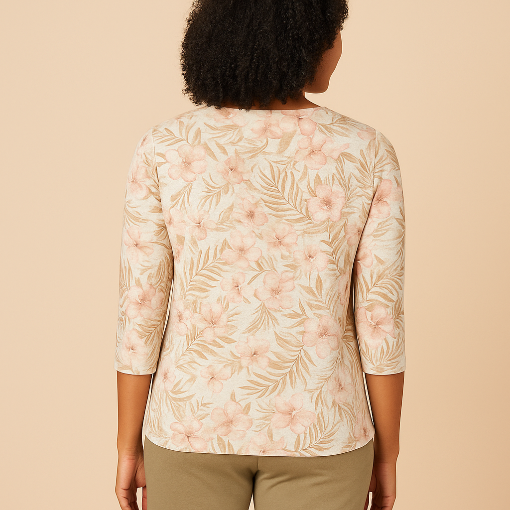 Back view for an African American woman with shoulder-length curly hair, smiling warmly while wearing a Comfort Code Baby French Terry Asymmetric Top in a soft floral print with blush and coral hues. She is paired with olive-green pants and stands against a soft beige background, highlighting the top’s asymmetric hem and delicate floral patterns for a fresh, elegant, and natural look.