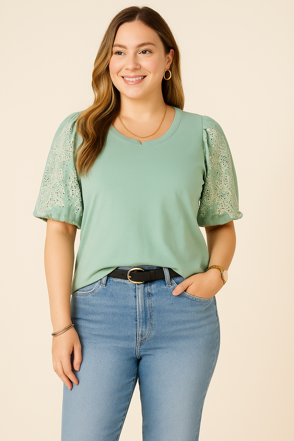 A young woman with fair skin models a Democracy Embroidered Puff-Sleeve Top in sage green, styled with trendy light blue high-waisted jeans. The top features delicate lace embroidery on the puff sleeves, paired with a black leather belt, gold hoop earrings, a gold chain necklace, and a classic wristwatch, creating a stylish and polished look.